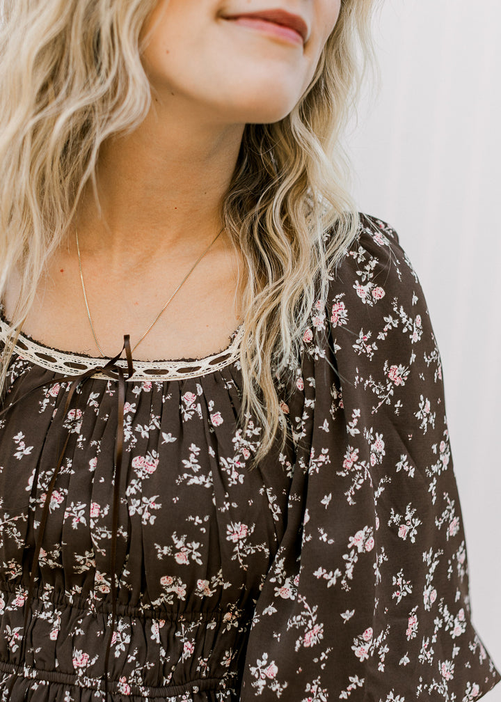 Close up of cream lace with brown tie at the scoop neck of a brown dress with pink floral. 