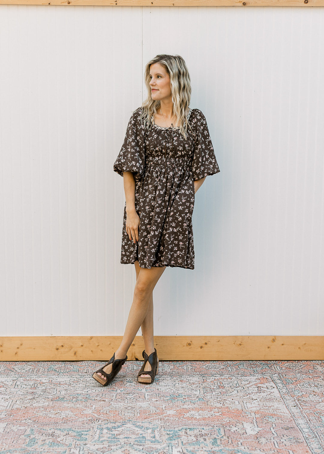 Model wearing wedges and a brown above the knee dress with elastic waist, 3/4 sleeves and pockets. 