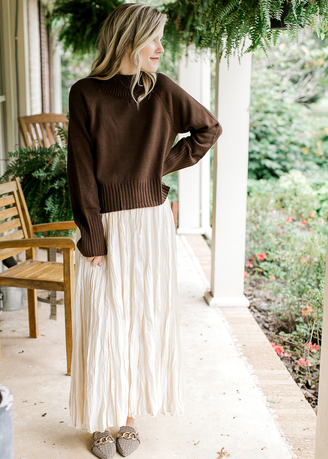 Model wearing a brown knit sweater with a mock neckline and long sleeves with ribbing detail.