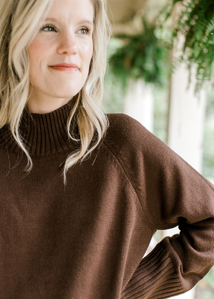Close up of mock neckline on a brown long sleeve sweater with ribbing at neck, cuff and hem.