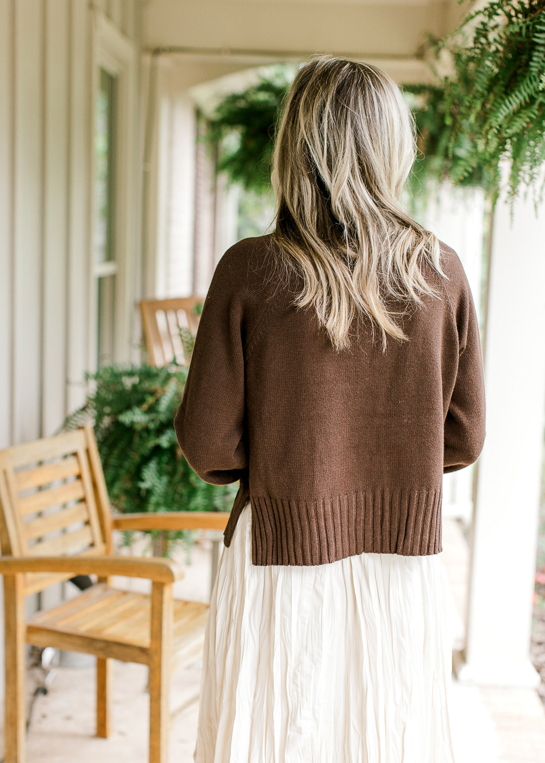 Back view of Model wearing a brown sweater with a mock neck and long sleeves with ribbing detail.