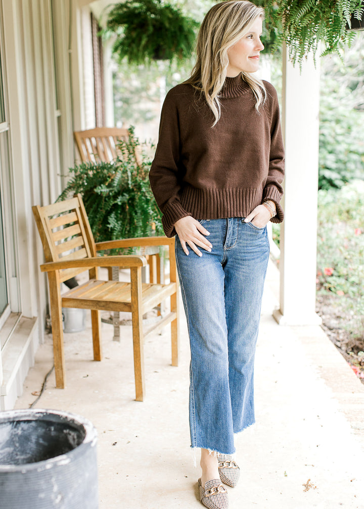 Model wearing jeans, flats and a brown sweater with a mock neck and long sleeves.