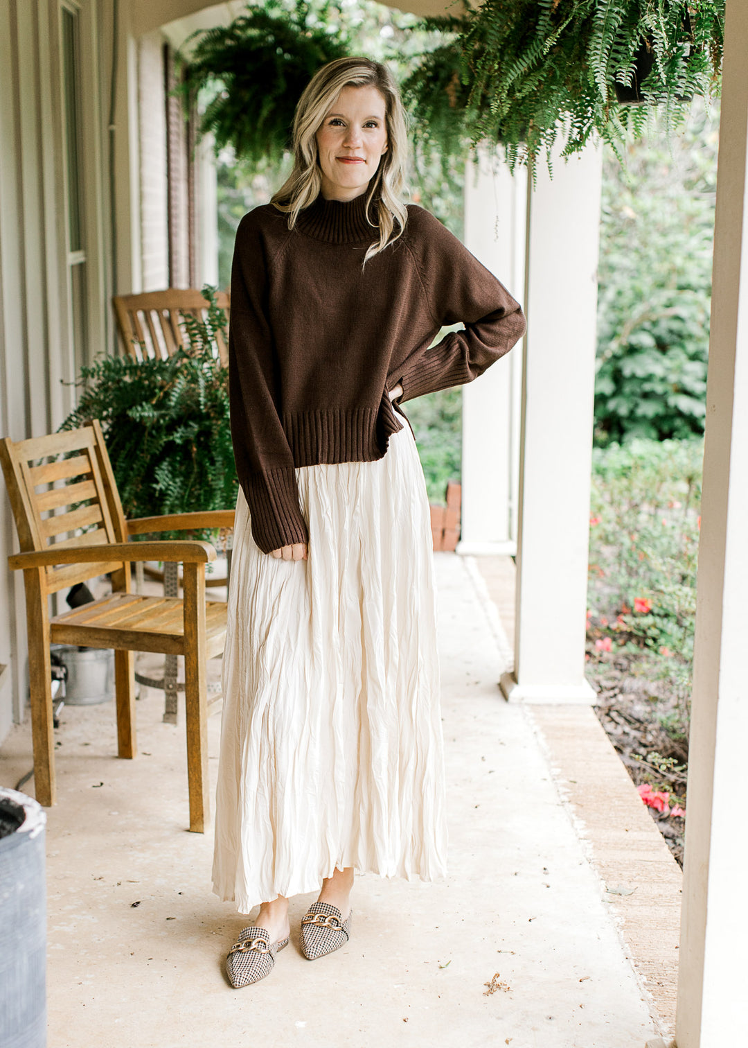 Model wearing cream maxi, flats and a brown sweater with a mock neck and long sleeves.