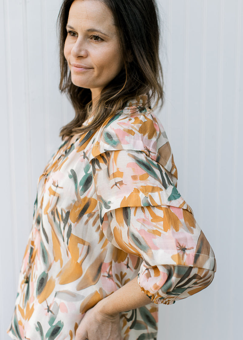 Model wearing a cream top with watercolor floral, tiered 3/4 sleeves and tie neck.