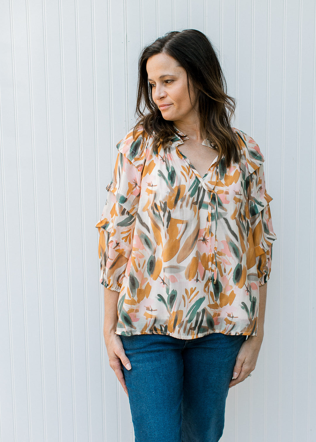 Model wearing a cream top with watercolor floral, v-neck with tie and 3/4 sleeves.