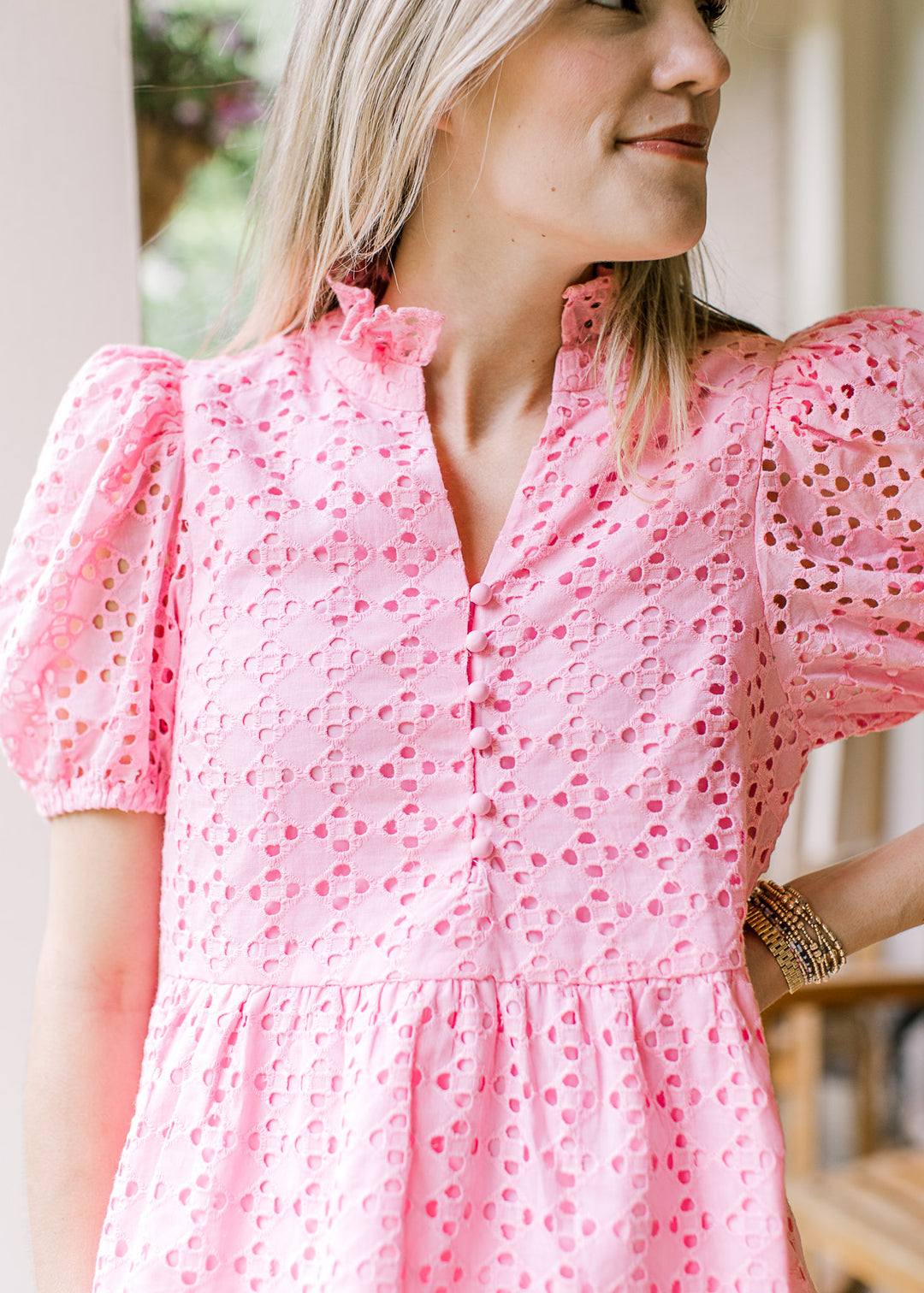 Model wearing a bubble gum pink top with short sleeves, v-neck with button and eyelets. 