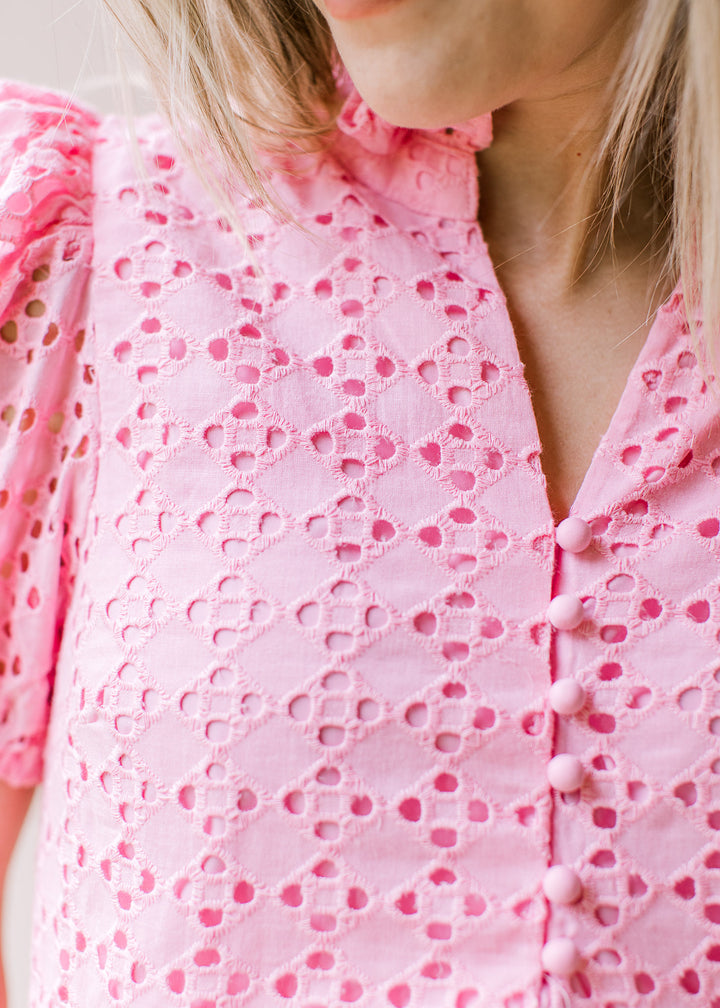 Close up of eyelets, pleated shoulders and v-neck with buttons on a bubble gum pink top. 
