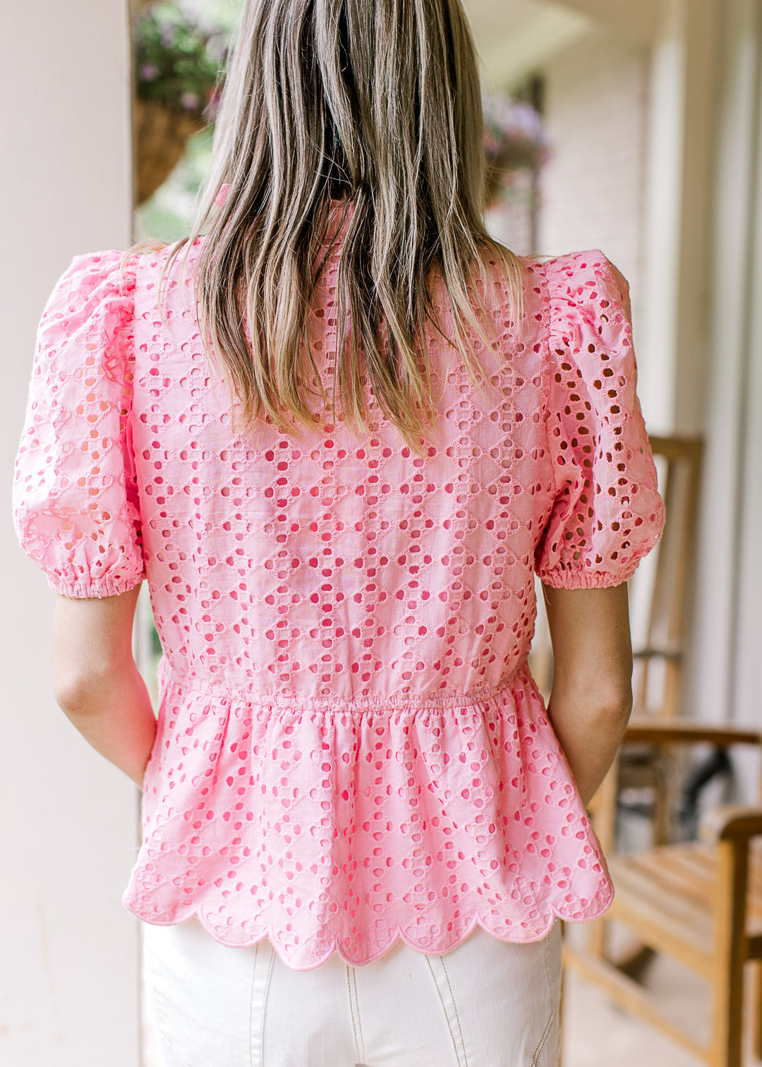 Back view of Model wearing a bubble gum pink top with short sleeves, scalloped hem and eyelets. 