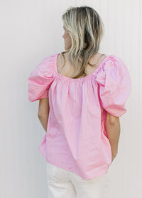 Back view of Model wearing a pink top with micro pleating and short elastic sleeves.