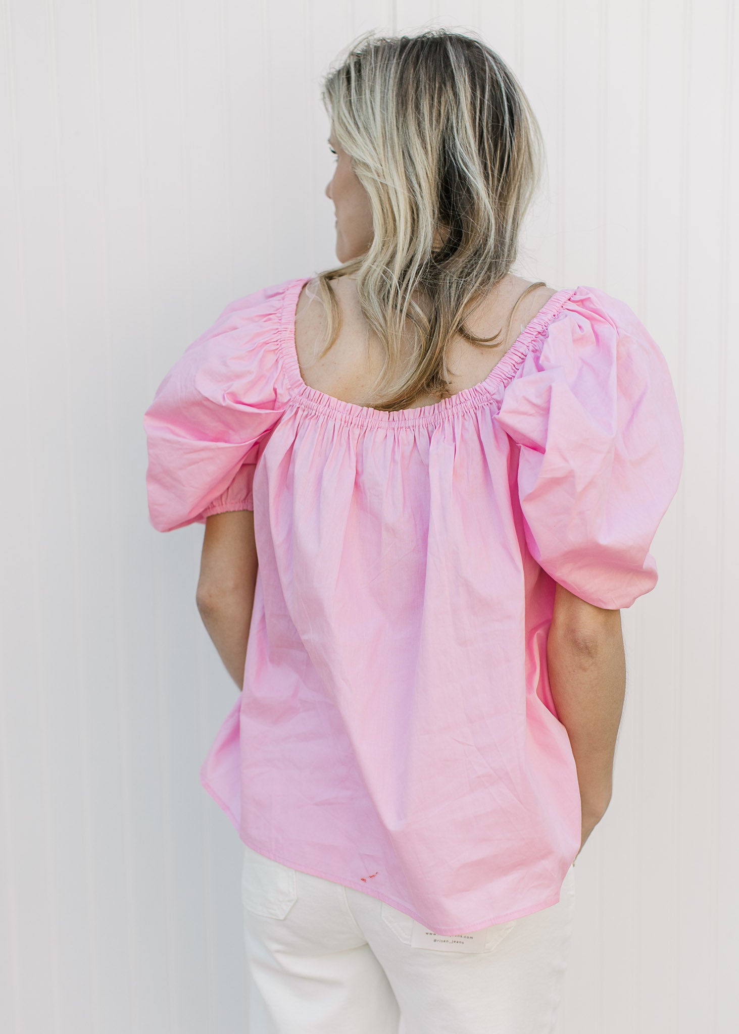 Back view of Model wearing a pink top with micro pleating and short elastic sleeves.