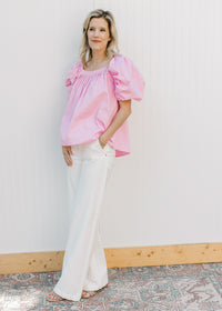Model wearing white jeans and a pink top with micro pleated bodice and back and short sleeves.
