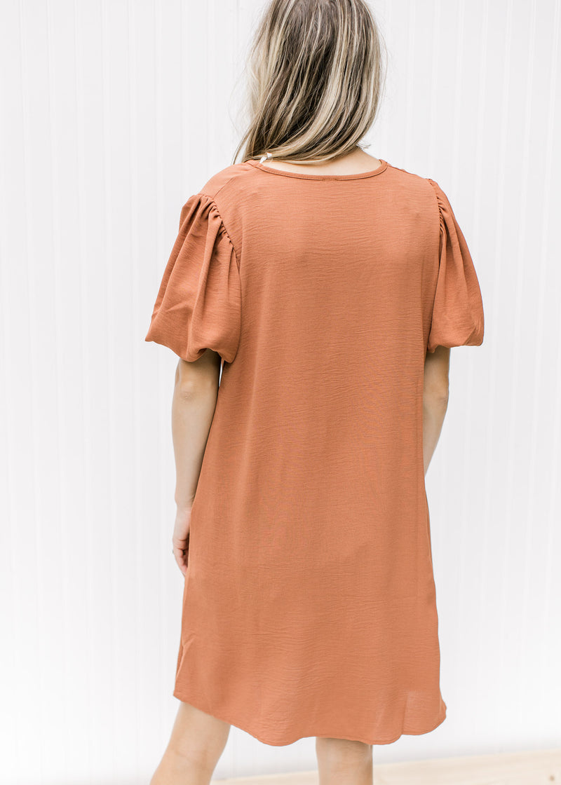 Back view of Model wearing a rust colored above the knee dress with bubble short sleeves. 