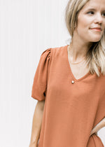Close up of v-neck and bubble short sleeves on a rust colored dress with pockets. 