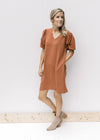 Model wearing booties with a rust colored above the knee dress with bubble short sleeves and pockets