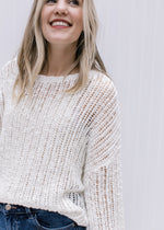 Model wearing a open knit sweater with a neutral color, long sleeves and a round neckline. 
