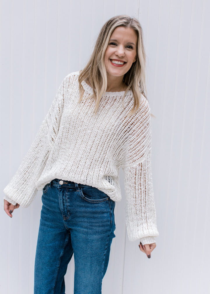 Model wearing jeans and a open knit sweater with a neutral color, long sleeves and a round neckline.