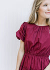 Close up of elastic waist and bubble short sleeves on a burgundy above the knee dress. 