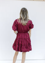Back view of Model wearing a burgundy above the knee dress with bubble short sleeves and hem. 