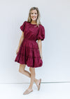 Model wearing flats with a burgundy above the knee dress with bubble short sleeves and hem. 