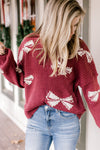 Model wearing jeans with a burgundy sweater with cream bows that are embellished with pearl beads. 