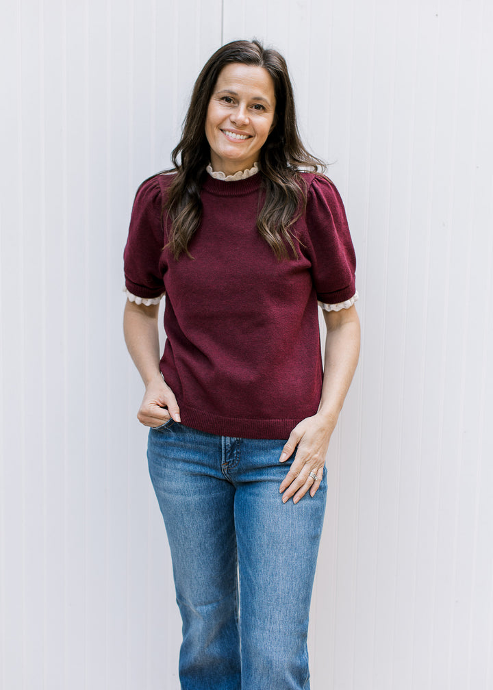 Model wearing the Burgundy Crochet Layer Top with blue jeans, showing its short puff sleeves and cream layered-look trim.
