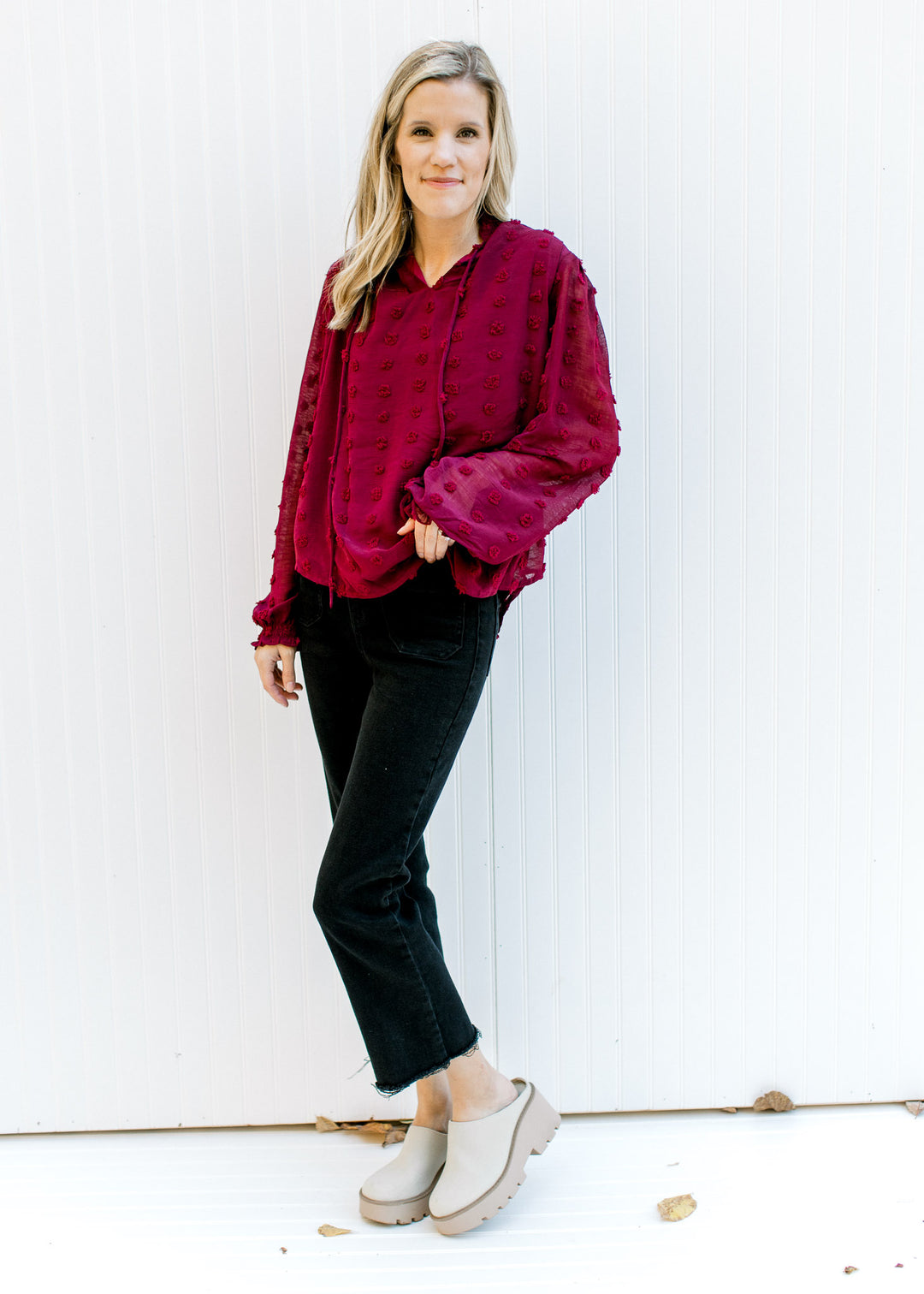Model wearing black jeans, mules and a wine dotted Swiss top with sheer sleeves and a mock neck. 