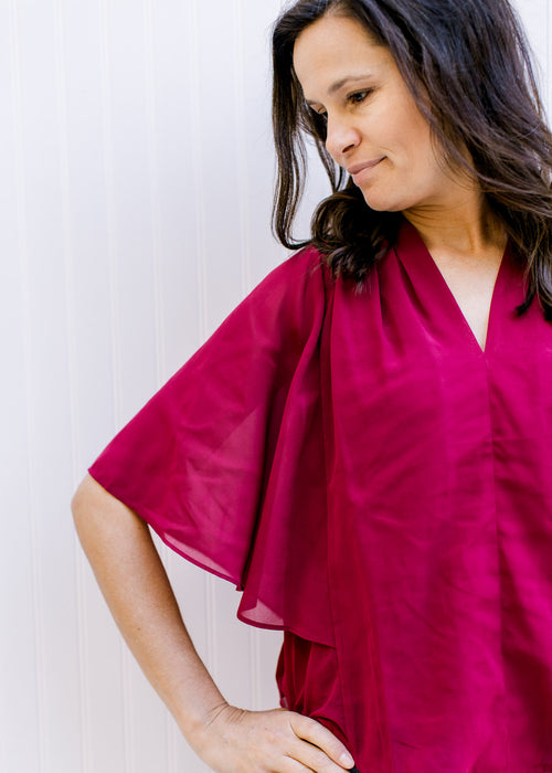 Model wearing a fully lined, burgundy blouse with kimono sleeves and v-neck. 
