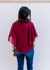 Back view of Model wearing a fully lined, burgundy blouse with kimono sleeves and v-neck. 