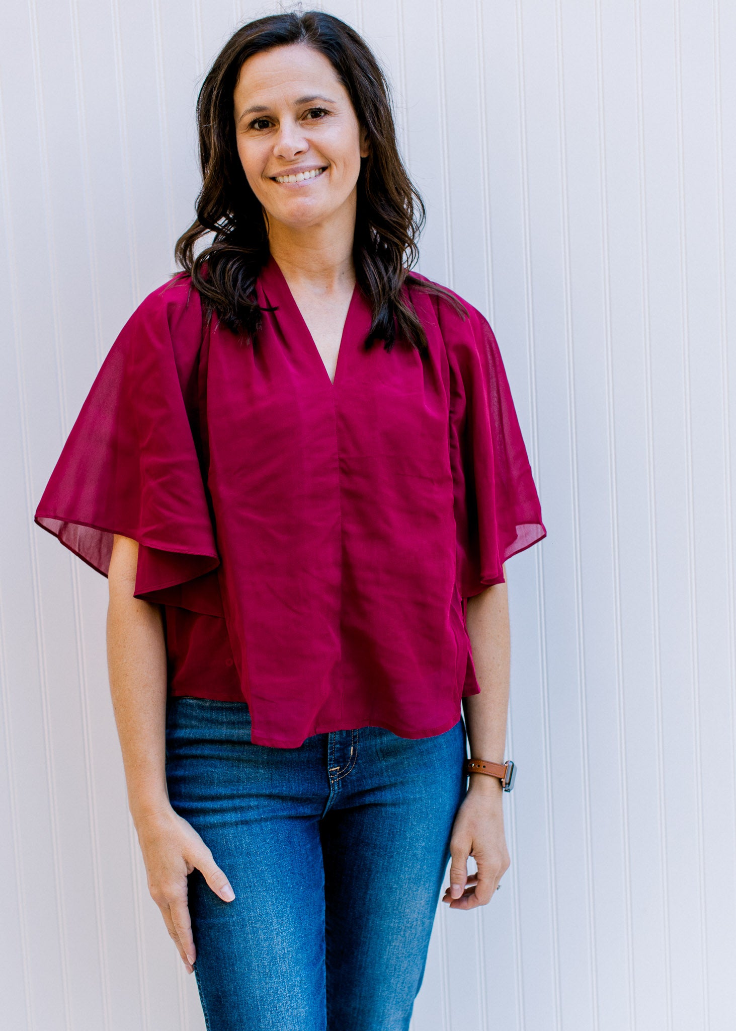 Model wearing jeans with a fully lined, burgundy blouse with kimono sleeves and v-neck. 