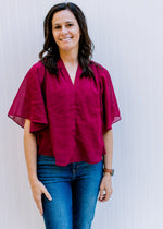 Model wearing jeans with a fully lined, burgundy blouse with kimono sleeves and v-neck. 