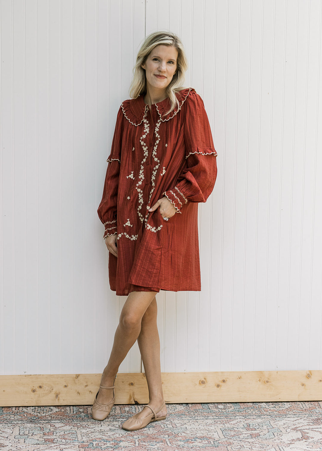 Model wearing a long sleeve burgundy dress with cream floral, pockets and exaggerated collar. 