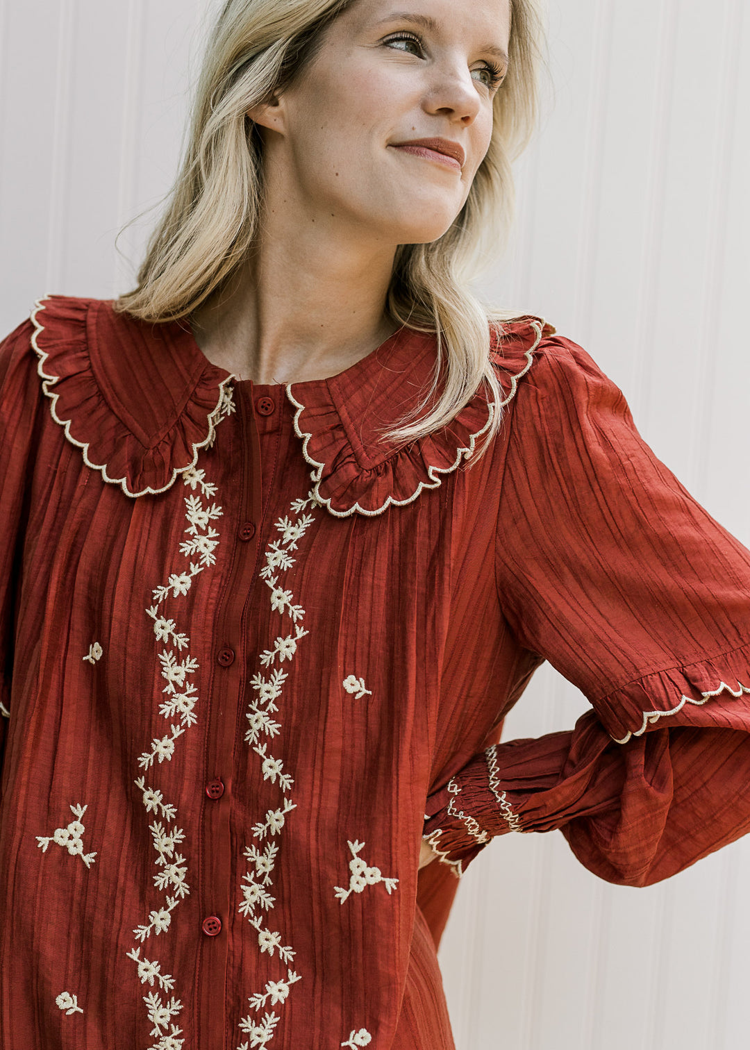 Close up on exaggerated collar with ruffles and cream embroidered flowers on a burgundy dress. 