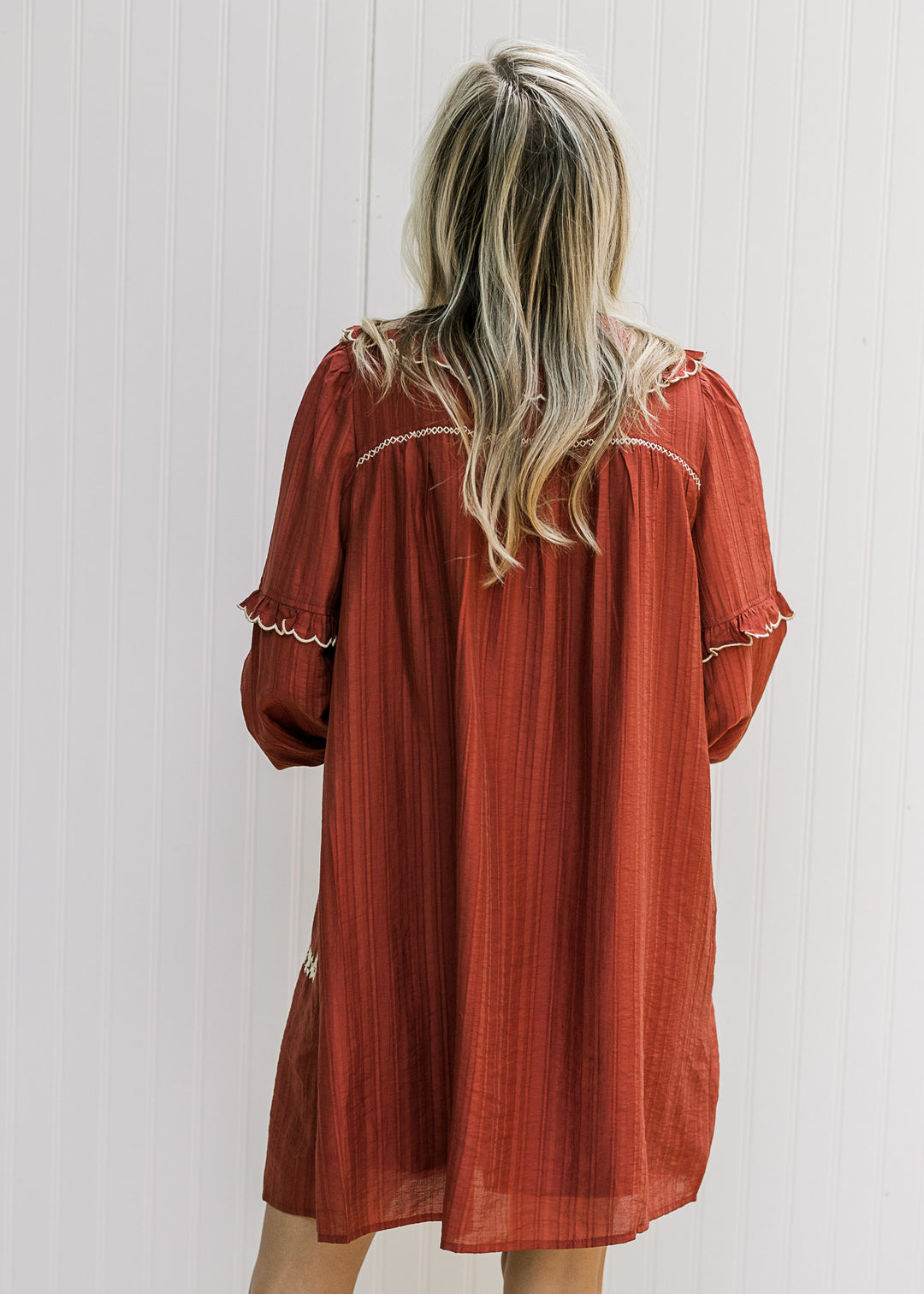 Back view of Model wearing a burgundy above the knee dress with cream ruffle tiers on sleeves.