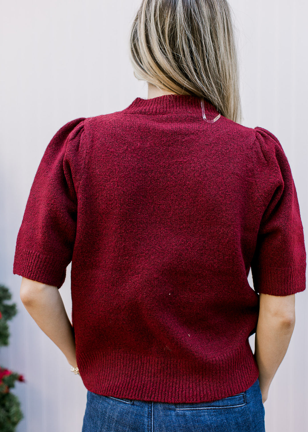 Back view of Model wearing a burgundy sweater with a round neck and short sleeves with pleating. 