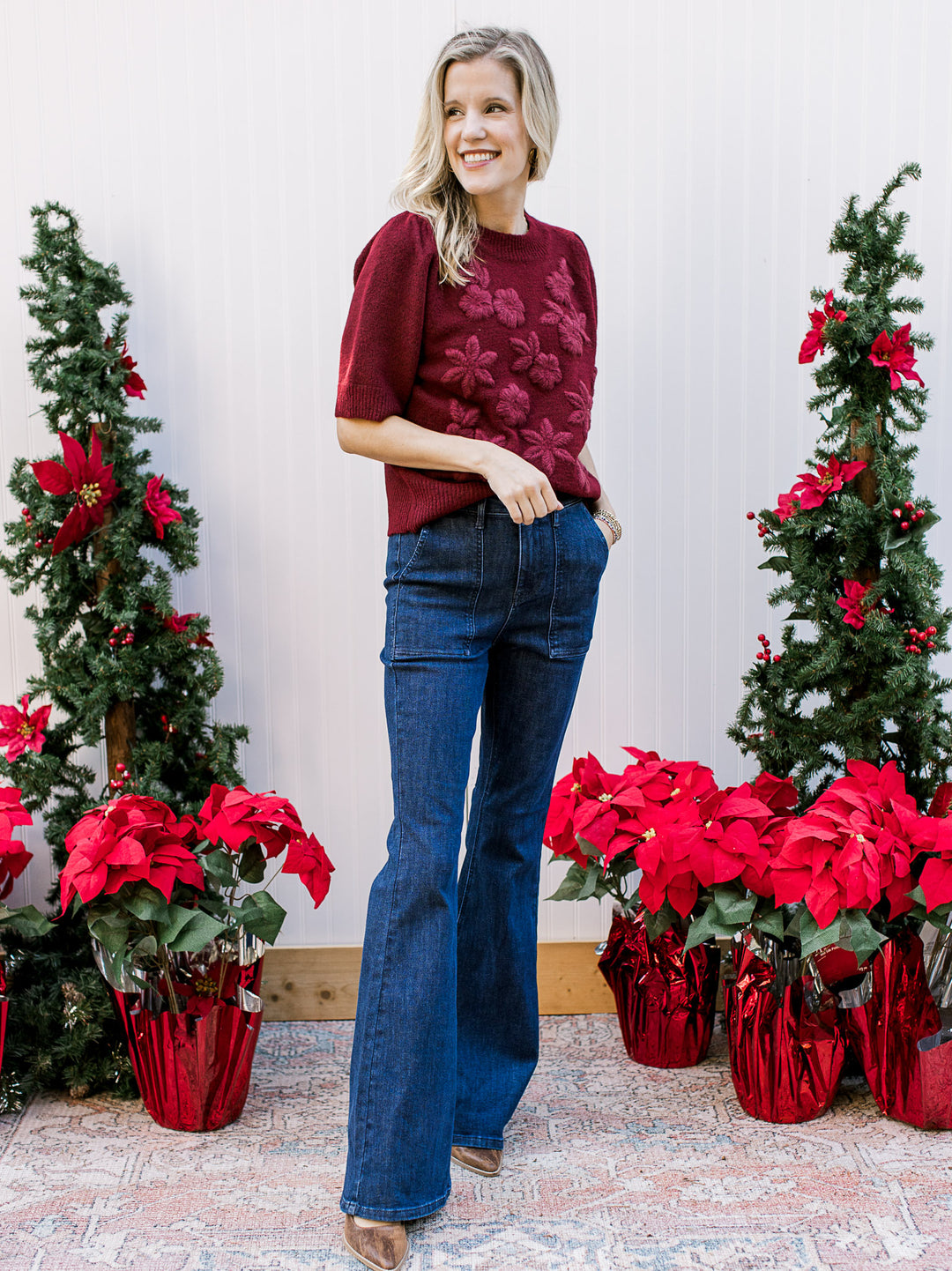 Model wearing a burgundy sweater with 3D flowers, short sleeves and a round neckline. 