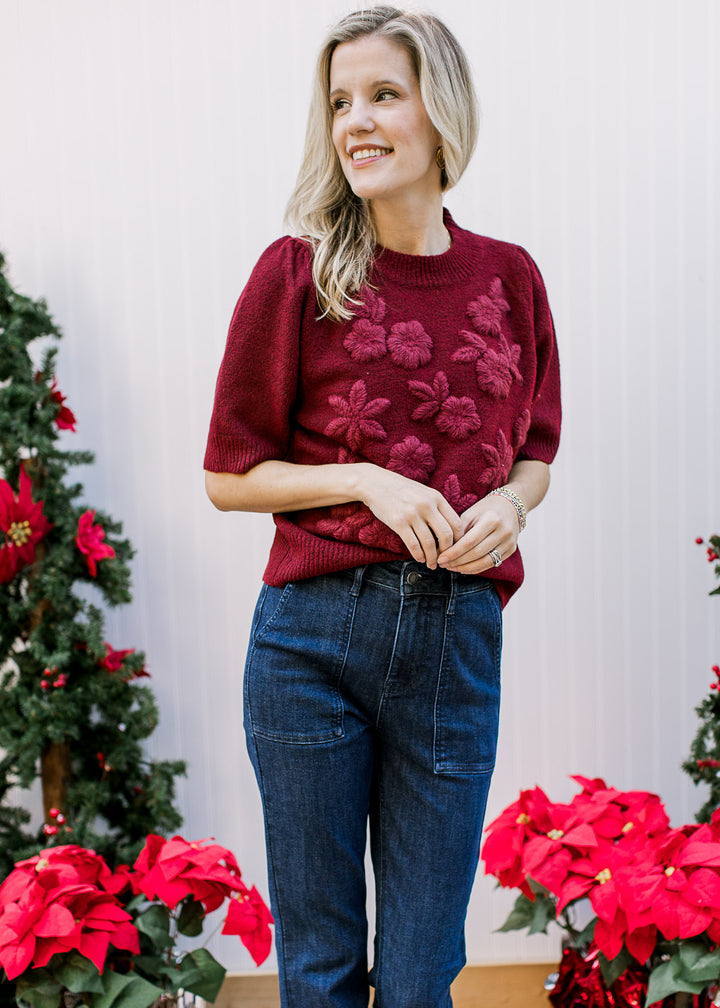 Model wearing a burgundy sweater with 3D flowers, pleated shoulder short sleeves and a round neck.