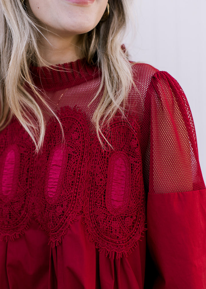 Close up of lace mock neckline and mesh neck and shoulders of an above the knee burgundy dress. 