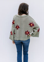 Back view of model wearing a sage sweater with burgundy flowers, exposed hem and long sleeves. 