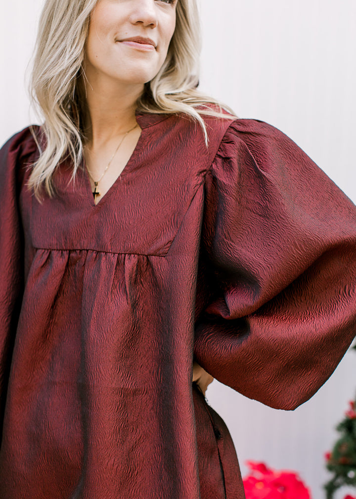 Close up of textured burgundy material and v-neck on an above the knee dress with long sleeves. 