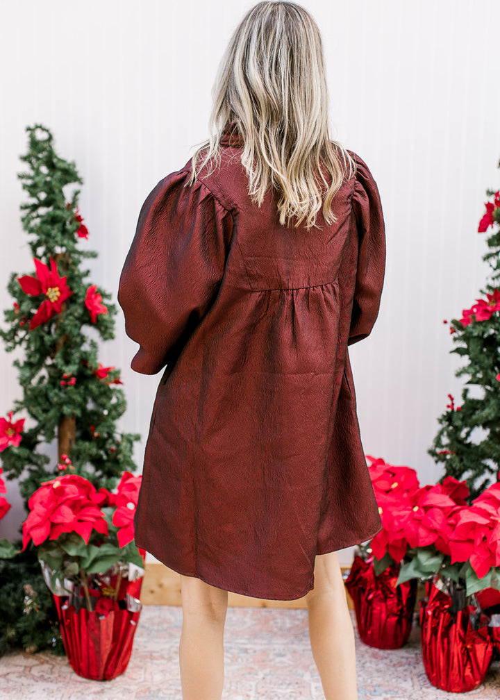 Back view of Model wearing a burgundy above-the-knee dress with a v-neck and bubble 3/4 sleeves.