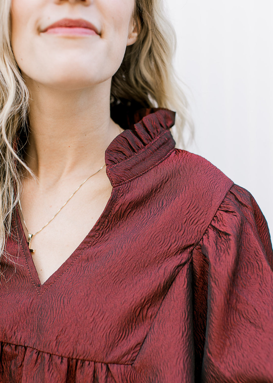 Close up of v-neck, pleated shoulders and ruffle at neck of a burgundy above the knee dress. 