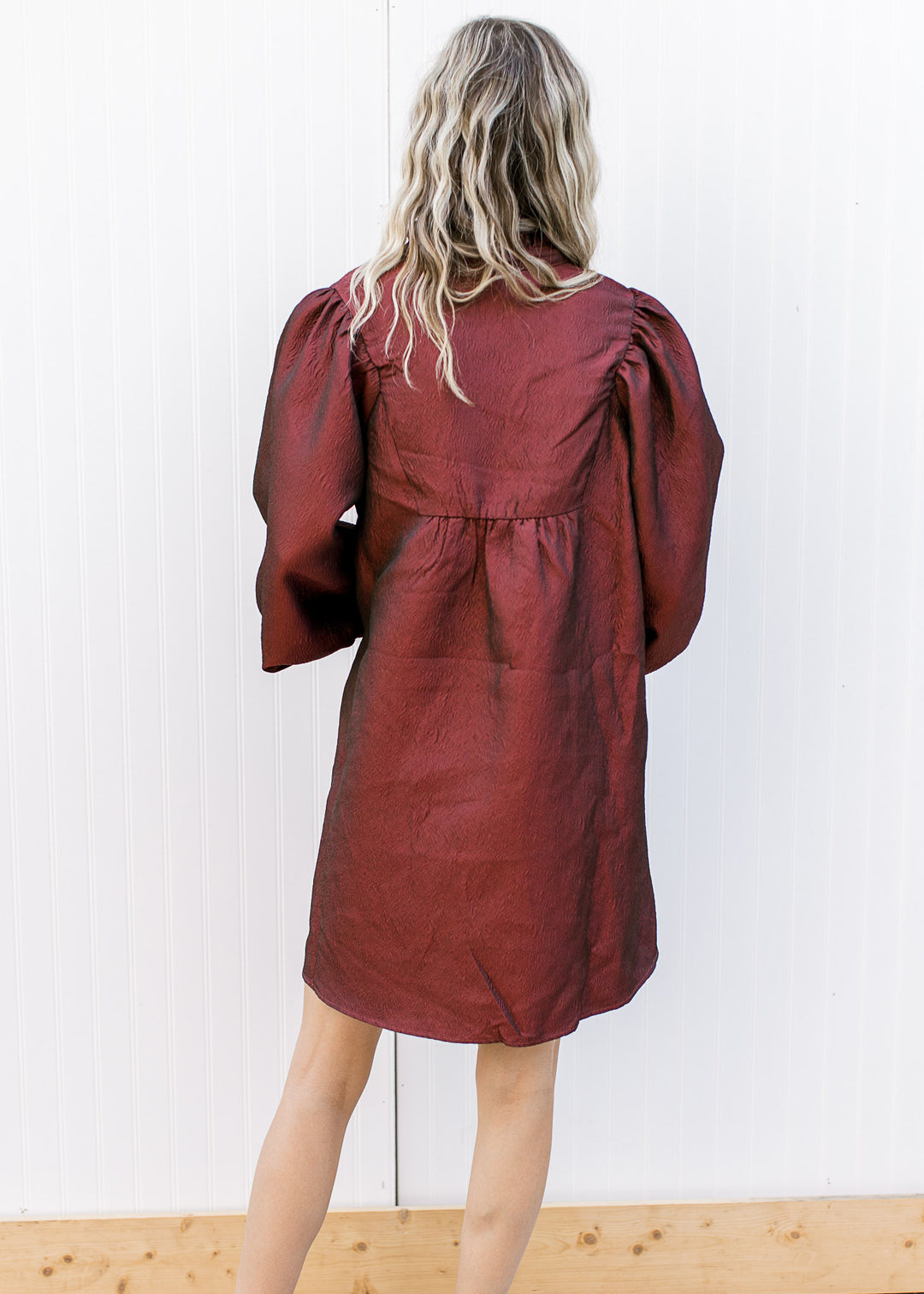 Back view of Model wearing a burgundy dress with a v-neck, 3/4 bubble sleeves and ruffle neck.
