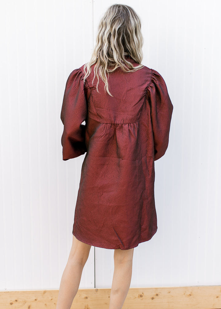 Back view of Model wearing a burgundy dress with a v-neck, 3/4 bubble sleeves and ruffle neck.