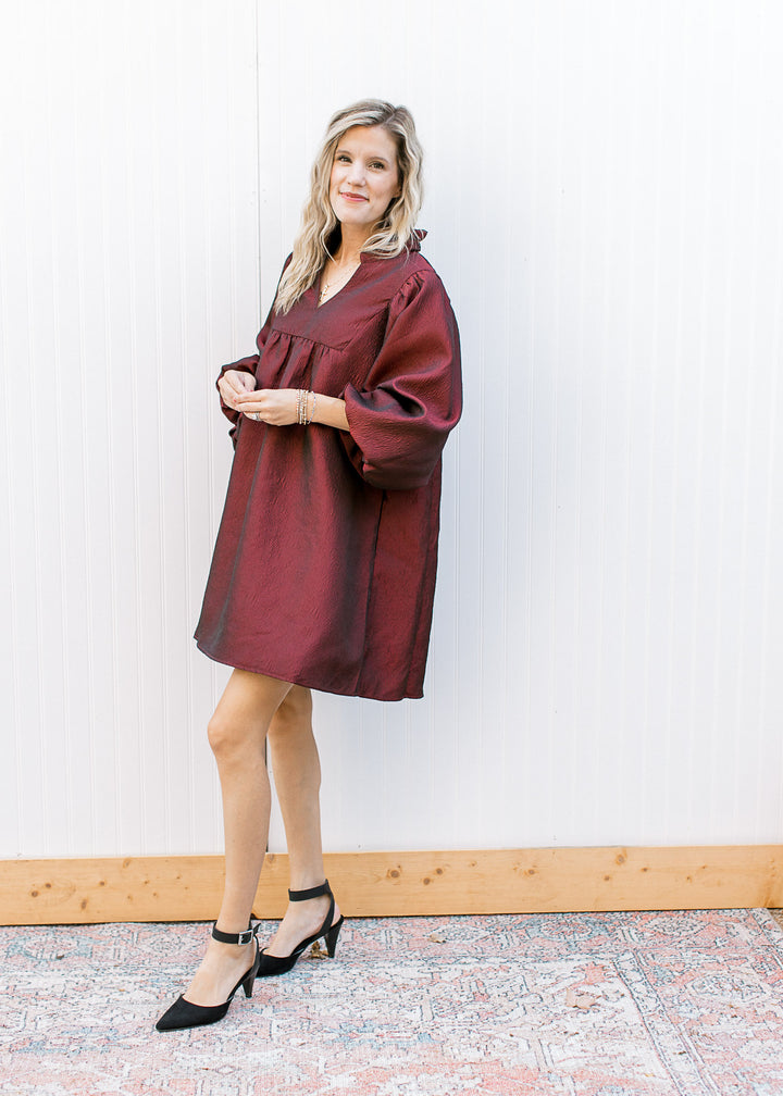 Model wearing a burgundy dress with a v-neck, 3/4 bubble sleeves and ruffle neck.