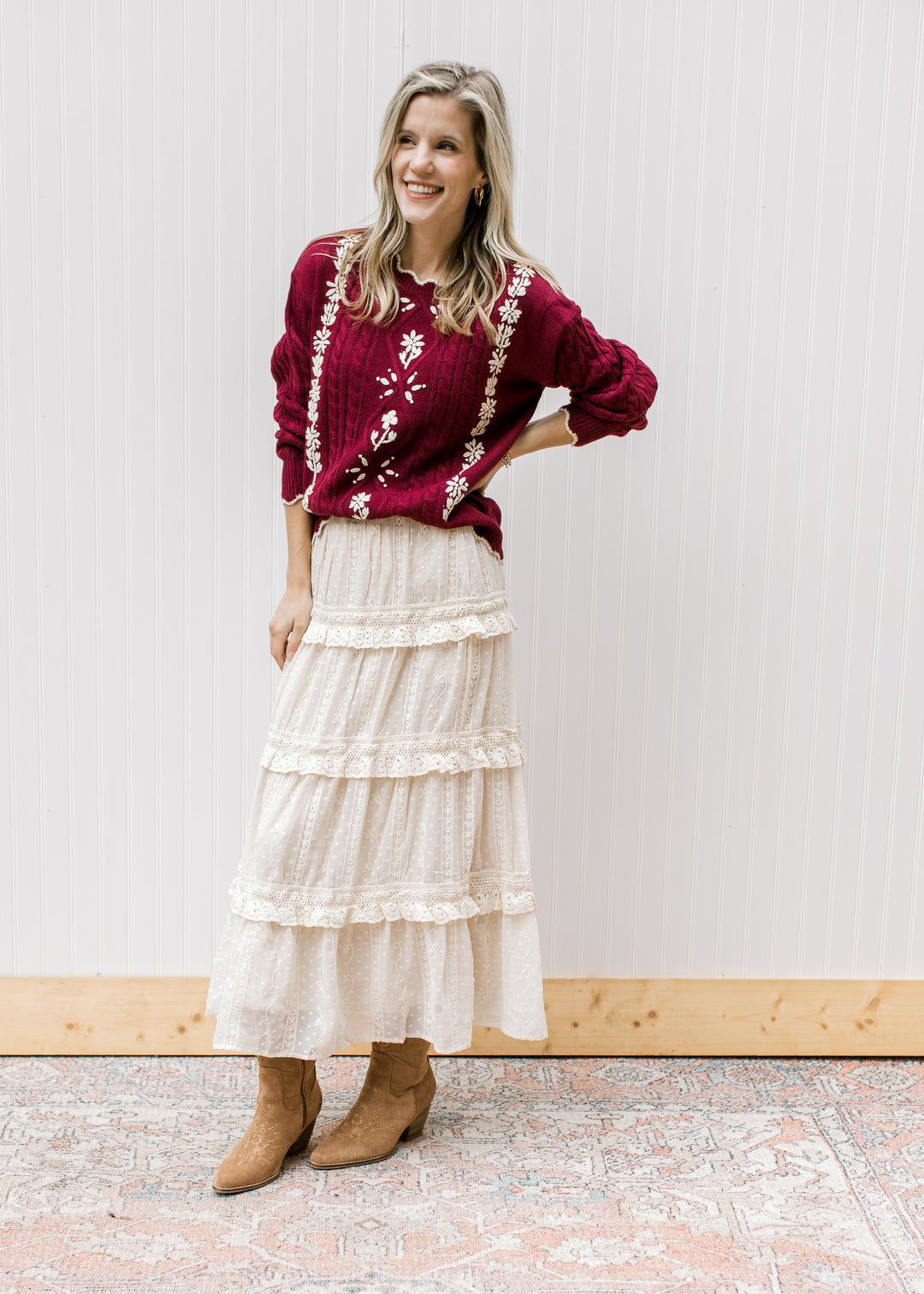 Model wearing a burgundy long sleeve cable knit sweater with cream floral and scalloping detail. 