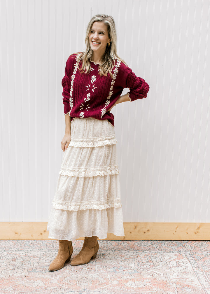 Model wearing a burgundy long sleeve cable knit sweater with cream floral and scalloping detail. 