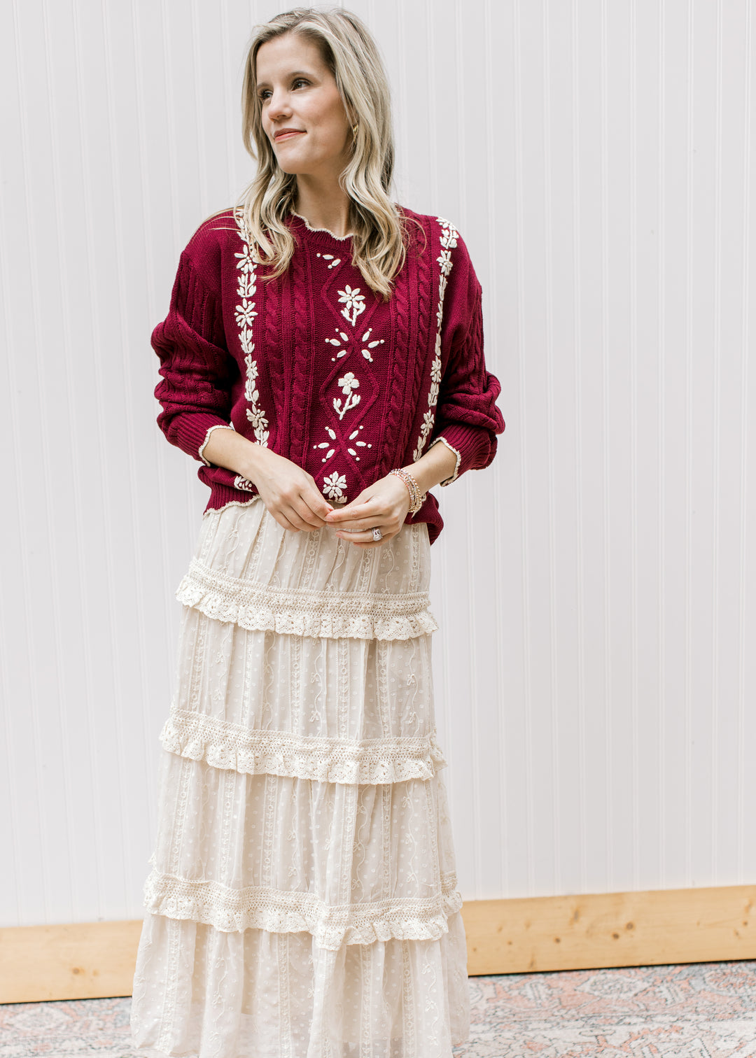 Model wearing cream skirt with a burgundy cable knit sweater with cream floral and long sleeves.