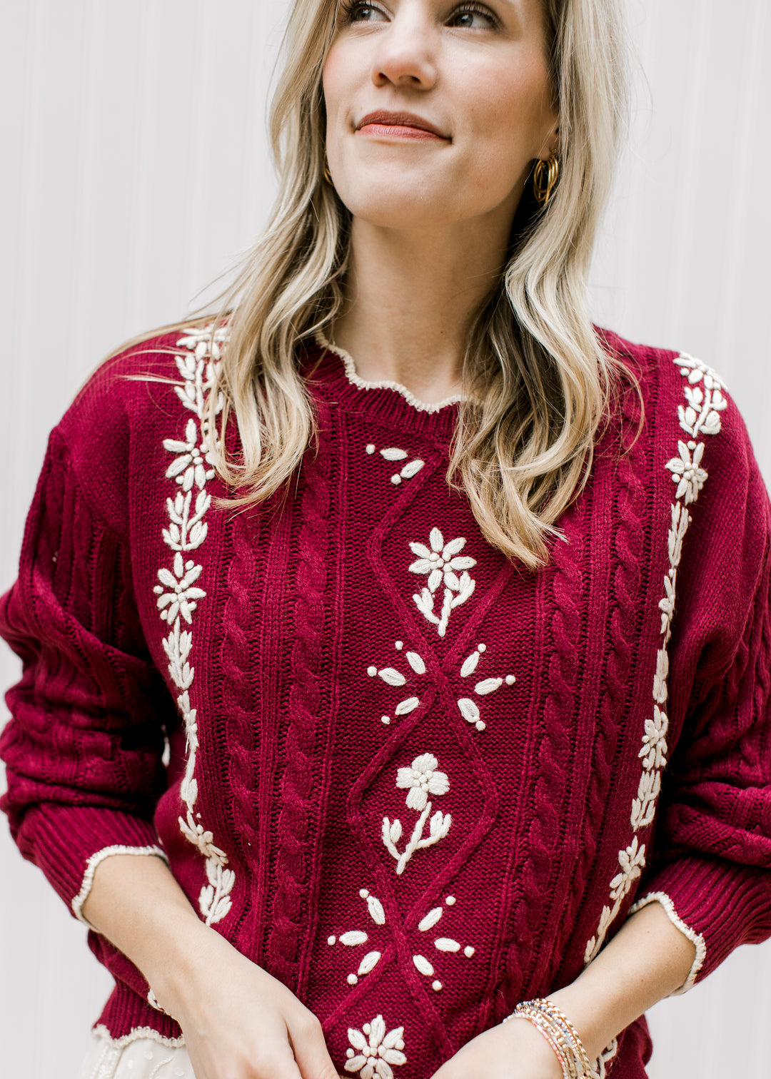 Close up of cream floral and scalloping at neck and sleeves of a burgundy long sleeve sweater. 