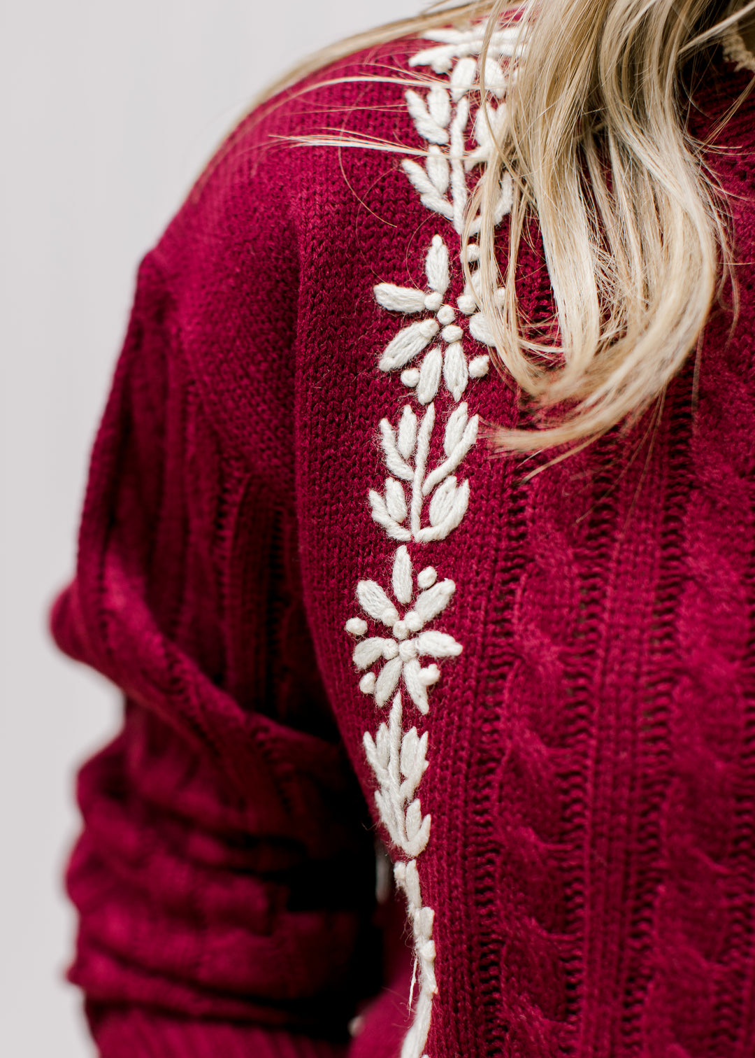Close up of cream floral detail on a burgundy cable knit sweater with long sleeves. 