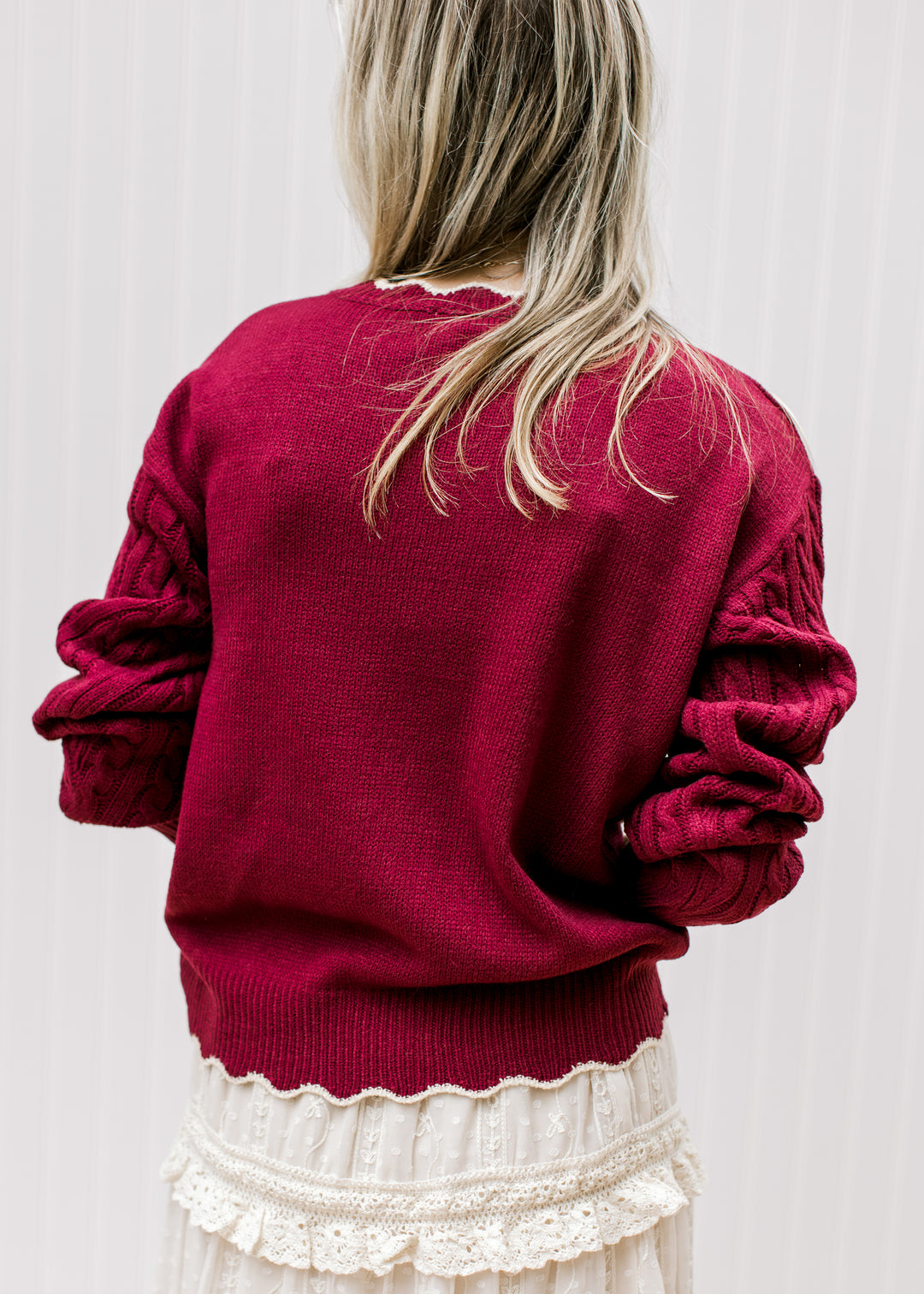 Back view of Model wearing a burgundy long sleeve sweater with cream floral and scalloping. 
